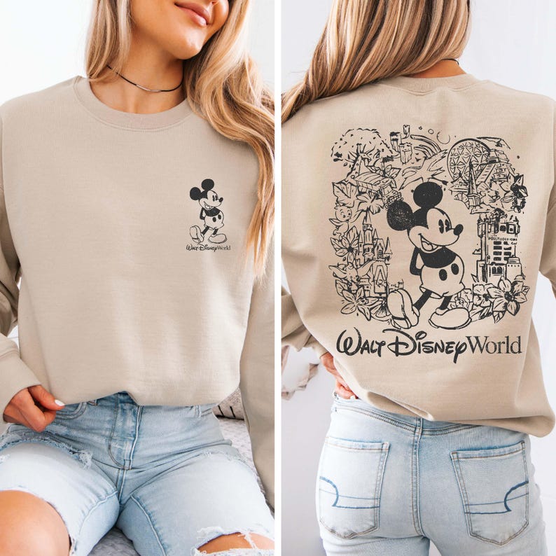 May include: A tan sweatshirt with a black and white Mickey Mouse graphic on the front and a black and white Mickey Mouse graphic with a "Walt Disney World" text on the back. The sweatshirt is being worn by a person with light brown hair and blue jeans.