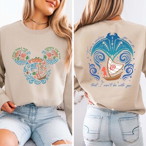 May include: A beige sweatshirt with a Mickey Mouse silhouette design featuring a Moana theme. The front of the sweatshirt has a Mickey Mouse silhouette with a Moana design inside. The back of the sweatshirt has a Moana design with the text "There is nowhere you can go that I won't be with you."