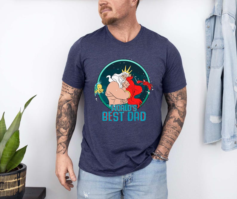 May include: A navy blue t-shirt with a graphic of King Triton and Ariel from The Little Mermaid. The graphic is surrounded by a blue circle with stars and the text "World's Best Dad".