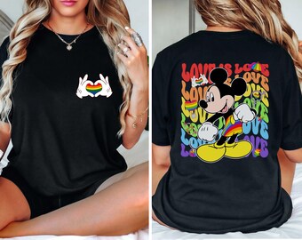Op de afbeelding: Zwart T-shirt met een regenboog hart in een handgebaar op de voorkant en een regenboog Mickey Mouse met de tekst "Love is Love" op de achterkant.