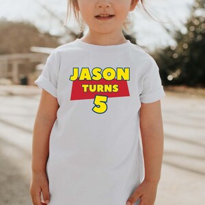 May include: A white short-sleeved t-shirt featuring a graphic print on the chest. The design includes the text JASON in yellow letters, the word TURNS in white letters on a red background, and the number 5 in large yellow digits with a blue outline.