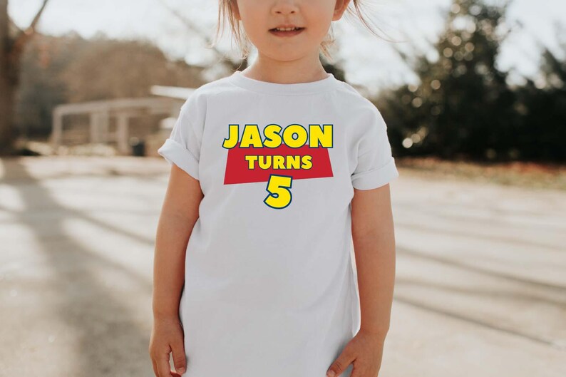 May include: A white short-sleeved t-shirt featuring a graphic print on the chest. The design includes the text JASON in yellow letters, the word TURNS in white letters on a red background, and the number 5 in large yellow digits with a blue outline.