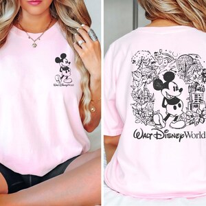 May include: Pink t-shirt with a black and white Mickey Mouse graphic on the front and a larger black and white Mickey Mouse graphic with a park scene on the back. The text "Walt Disney World" is printed on the back of the shirt.