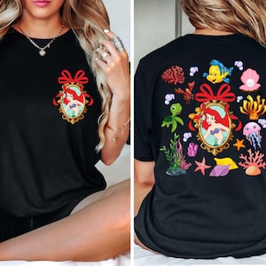 May include: Black t-shirt with a red bow and a picture of Ariel from The Little Mermaid on the front. The back of the shirt has a variety of sea creatures and plants, including a turtle, a crab, a starfish, and a jellyfish.