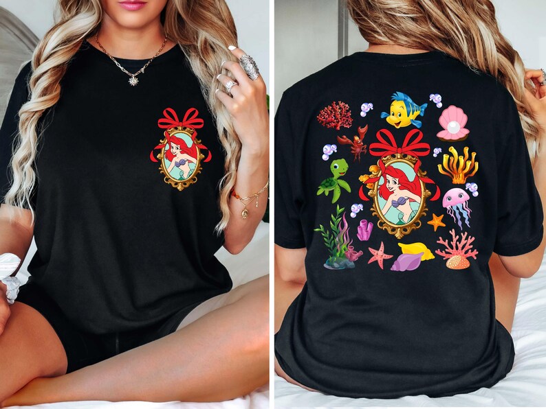 May include: Black t-shirt with a red bow and a picture of Ariel from The Little Mermaid on the front. The back of the shirt has a variety of sea creatures and plants, including a turtle, a crab, a starfish, and a jellyfish.
