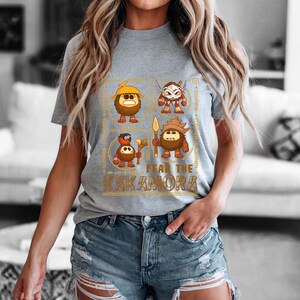 May include: A gray t-shirt featuring a graphic design with four cartoon characters and the text "FEAR THE KAKAMORA" in gold. The characters are brown with various accessories and weapons.