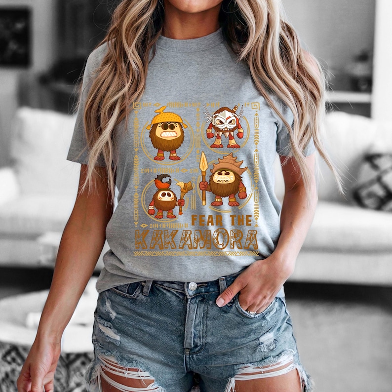 May include: A gray t-shirt featuring a graphic design with four cartoon characters and the text "FEAR THE KAKAMORA" in gold. The characters are brown with various accessories and weapons.