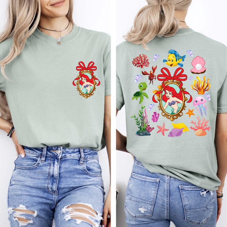 May include: Two light green t-shirts with a cartoon image of Ariel from The Little Mermaid. One shirt has a single image of Ariel in a frame with a red bow. The other shirt has multiple images of Ariel, sea creatures, and seashells.