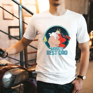 May include: White t-shirt with a graphic of King Triton from The Little Mermaid hugging Ariel. The graphic is in a circle with a blue background and stars. The text "World's Best Dad" is below the graphic.