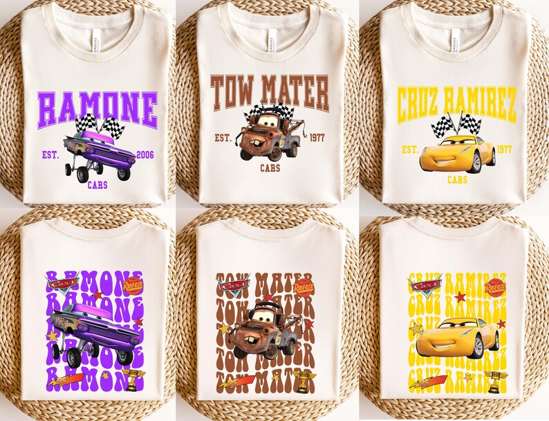 May include: Six off-white t-shirts with different designs featuring characters from the movie Cars. The designs include the names "Ramone", "Tow Mater", and "Cruz Ramirez" with associated graphics and text. The shirts are arranged on a woven surface.