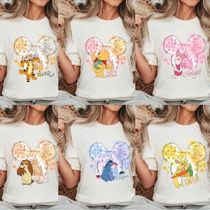 May include: Cream-colored t-shirts featuring Disney characters within a Mickey Mouse head design. Characters include Tigger, Winnie the Pooh, Piglet, Owl, Eeyore, and Rabbit. Each design has a unique color scheme and character name.