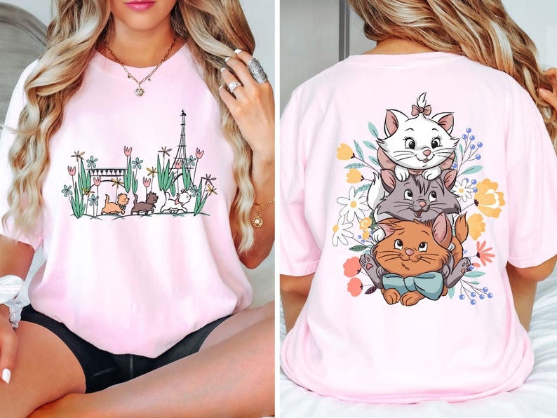 May include: Pink t-shirt with a graphic of three cats from the Disney movie The Aristocats. The cats are stacked on top of each other and surrounded by flowers. The front of the shirt has a graphic of the Eiffel Tower and three cats.