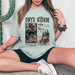 Puede incluir: Una camiseta azul claro con un estampado gr&aacute;fico de una ilustraci&oacute;n en blanco y negro de un castillo, un libro y una criatura. El texto "ONYX STORM" est&aacute; impreso en negro sobre el gr&aacute;fico. El texto "BASSGIATH WAR + COLLEGE" est&aacute; impreso en negro debajo del gr&aacute;fico. El texto "I Will Not Die To Day I Will Save Him" est&aacute; impreso en negro sobre el castillo.