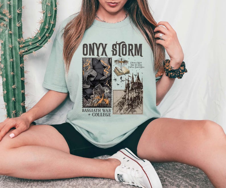 Puede incluir: Una camiseta azul claro con un estampado gr&aacute;fico de una ilustraci&oacute;n en blanco y negro de un castillo, un libro y una criatura. El texto "ONYX STORM" est&aacute; impreso en negro sobre el gr&aacute;fico. El texto "BASSGIATH WAR + COLLEGE" est&aacute; impreso en negro debajo del gr&aacute;fico. El texto "I Will Not Die To Day I Will Save Him" est&aacute; impreso en negro sobre el castillo.