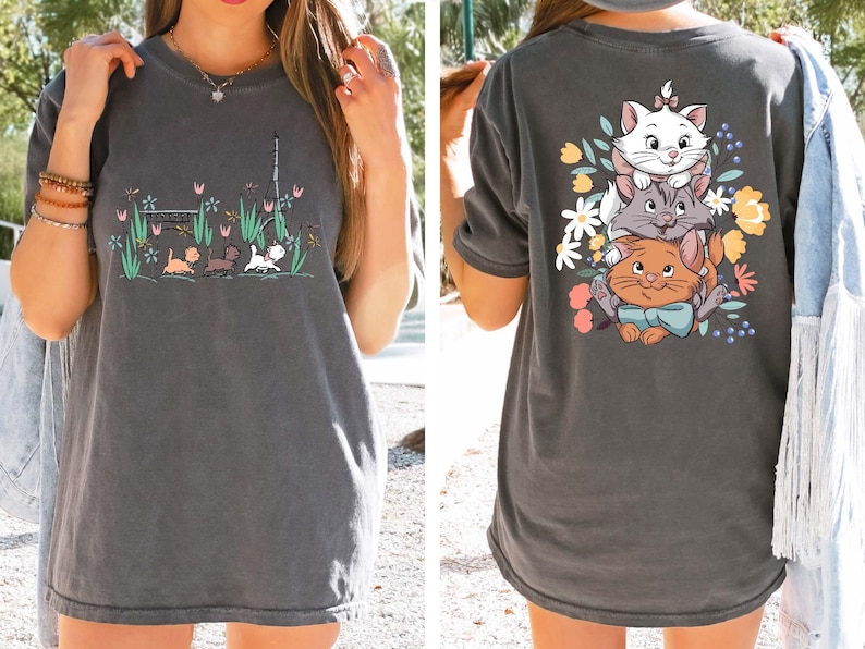 May include: A gray t-shirt with a cartoon image of three cats on the back. The cats are stacked on top of each other and surrounded by flowers. The front of the shirt has a cartoon image of three cats walking in a park.
