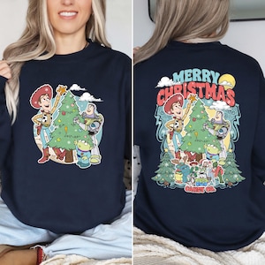 Puede incluir: Sudadera azul marino con un dise&ntilde;o de dibujos animados festivo que presenta a Woody, Buzz Lightyear y un extraterrestre decorando un &aacute;rbol de Navidad. La parte posterior de la sudadera tiene las palabras "Merry Christmas". El logotipo de Candy Co. tambi&eacute;n es visible.