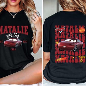 May include: Black t-shirt featuring a maroon car graphic with the name "Natalie" in a maroon arched font. The front design includes checkered flags and the text "Cars" and "Est. 2017". The back of the shirt has a similar design.