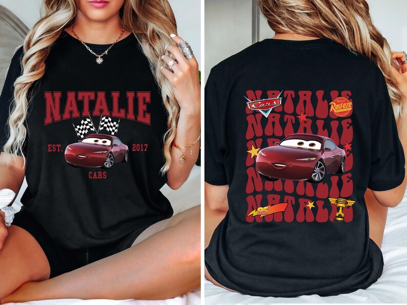 May include: Black t-shirt featuring a maroon car graphic with the name "Natalie" in a maroon arched font. The front design includes checkered flags and the text "Cars" and "Est. 2017". The back of the shirt has a similar design.