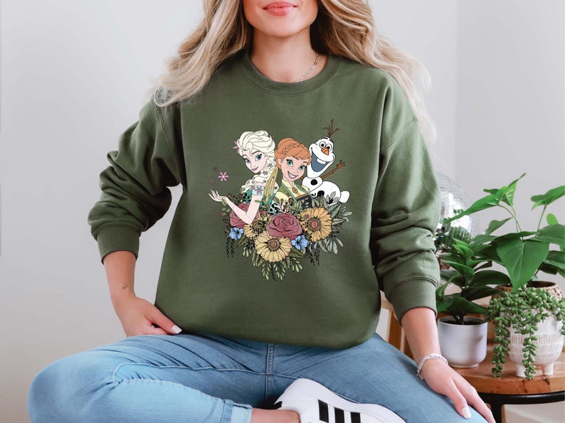 Pu&ograve; includere: Una felpa verde con un design floreale con i personaggi Elsa e Anna di Frozen, insieme a Olaf.