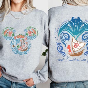 May include: Gray sweatshirt with a Mickey Mouse silhouette design featuring a Moana theme. The design includes a boat, waves, and the text "Come What May I Know The Way". The back of the sweatshirt has a blue and green design with a boat and the text "There is nowhere you can go that I won't be with you."