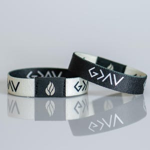 May include: Two black and white fabric wristbands with the word "God" written in a stylised font and a small leaf design.