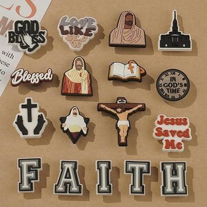 May include: A collection of religious-themed charms and embellishments. The charms include images of Jesus, crosses, and phrases like "God Bless," "Blessed," and "Jesus Saved Me." The word "FAITH" is spelled out in individual letter charms.