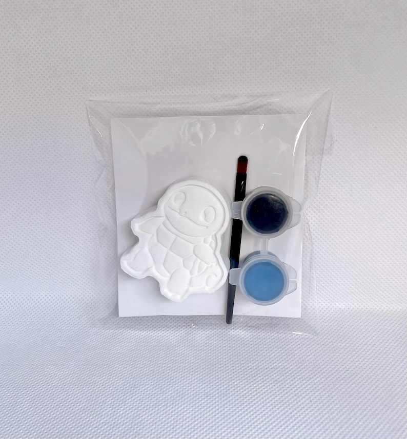 May include: A craft kit in a clear plastic bag containing a white turtle-shaped plaster figure, a thin black paintbrush, and two small circular containers of paint, one filled with dark blue paint and the other with light blue paint.