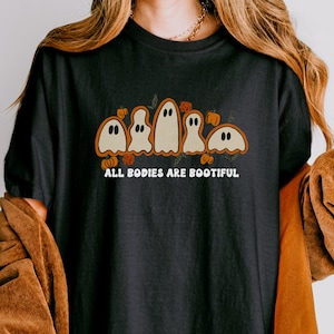 Comfort Colors® shirt with five different-shaped ghosts surrounded by pumpkins and flowers, featuring the phrase “All Bodies Are Bootiful” in bold white text.