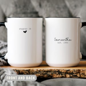 May include: Two white ceramic mugs with black handles and rims. One mug has "chapter 30" and a heart, the other has "Samantha EST. 1995". The mugs are on a wooden board.