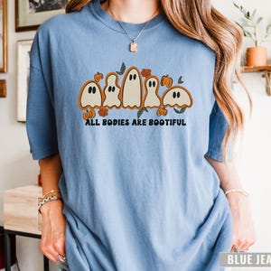 Comfort Colors® shirt with five different-shaped ghosts surrounded by pumpkins and flowers, featuring the phrase “All Bodies Are Bootiful” in bold black text