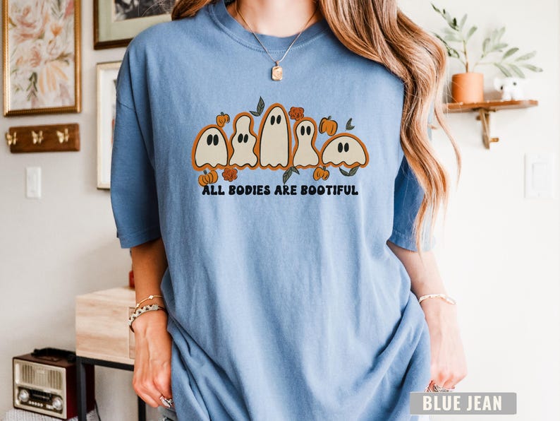 Comfort Colors® shirt with five different-shaped ghosts surrounded by pumpkins and flowers, featuring the phrase “All Bodies Are Bootiful” in bold black text