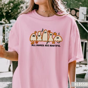 Comfort Colors® shirt with five different-shaped ghosts surrounded by pumpkins and flowers, featuring the phrase “All Bodies Are Bootiful” in bold black text