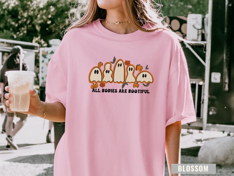 Comfort Colors® shirt with five different-shaped ghosts surrounded by pumpkins and flowers, featuring the phrase “All Bodies Are Bootiful” in bold black text