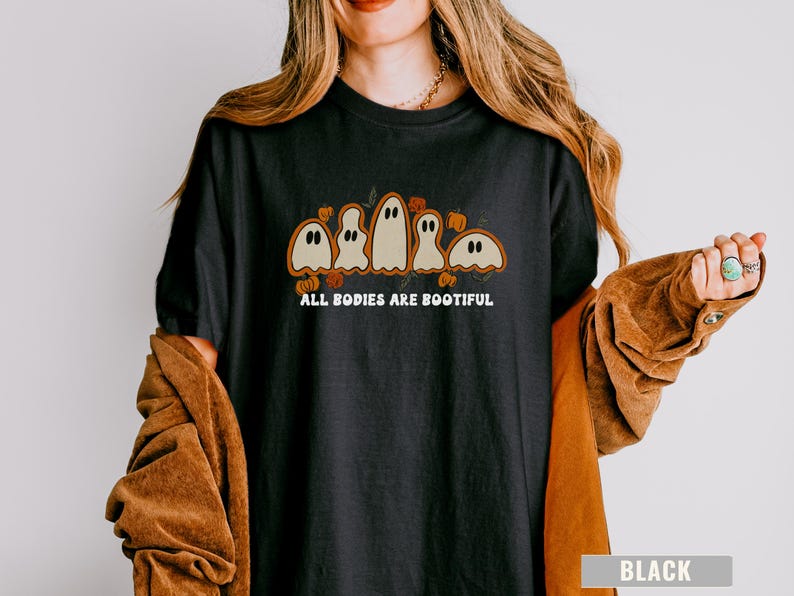Comfort Colors® shirt with five different-shaped ghosts surrounded by pumpkins and flowers, featuring the phrase “All Bodies Are Bootiful” in bold white text.