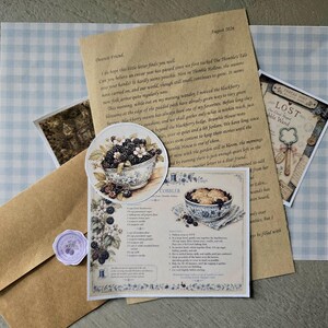 Puede incluir: Un conjunto de papelería que incluye una carta color canela fechada en agosto de 2026, una pegatina redonda con un cuenco de moras, una tarjeta de receta de cobbler de moras, una pequeña tarjeta rectangular titulada LOST y un sello de cera morado claro.