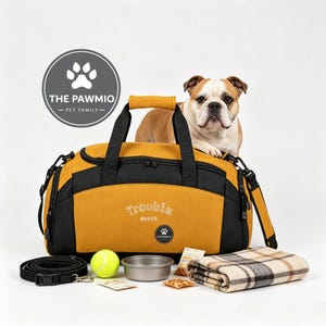May include: A mustard yellow and black duffel bag with the text Trouble Maker, a bulldog, a black lead, a yellow tennis ball, a metal bowl, two small food packets, and a folded beige and black plaid blanket. A circular logo reads The Pawmio.