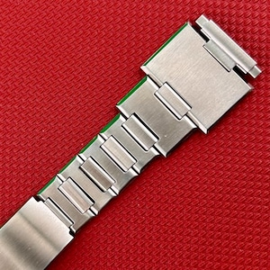 May include: A brushed stainless steel watch bracelet featuring a series of rectangular links and a secure folding clasp mechanism. The metal band has a smooth, matte finish with visible segments that connect to form a flexible, durable wrist strap.