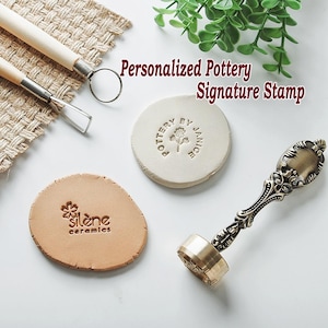 May include: An overhead shot shows pottery tools and stamps. A brass stamp with an ornate handle sits next to a clay stamp with the text "Pottery by Janice". The image also includes a clay piece stamped with "silène ceramics". The text "Personalized Pottery Signature Stamp" is visible.