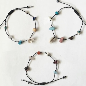 May include: Three black string bracelets with various colored beads and charms, including shells, stones, and a small piece of wood. The bracelets are adjustable with a sliding knot.