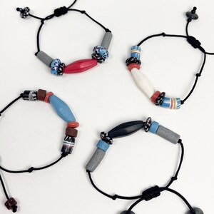 May include: Four bracelets with black cord and colorful beads. Each bracelet has a different combination of beads, including gray, red, blue, white, and black.