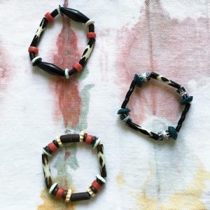 May include: Three bracelets made of black, white, and red beads. The bracelets are made of different materials, including wood and plastic.