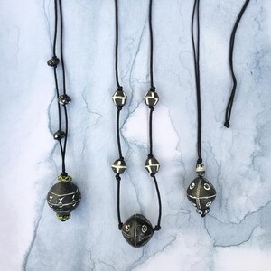 May include: Three black necklaces with black and white ceramic beads and pendants. The pendants are round and have a geometric design.