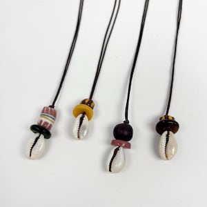 May include: Three necklaces with cowrie shells and colorful beads. Each necklace has a different combination of beads, including brown, yellow, pink, and green.