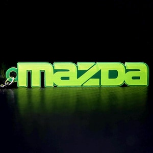 May include: A green plastic keychain with the word "mazda" in a stylized font.