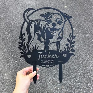 May include: Black metal garden stake featuring a Chihuahua dog design within a circular frame. The stake includes the name "Tucker" and the years "2010-2026". Decorative floral and heart accents are also present.