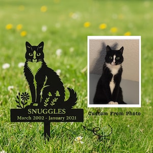 May include: A black metal cat memorial stake with the name "Snuggles" and dates March 2002 - January 2021. The stake features a silhouette of a cat and a photo of a black and white cat. The text "Custom From Photo" is also visible.
