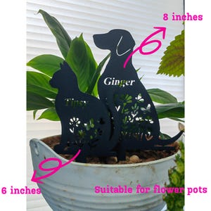 May include: Black metal cat and dog silhouette plant stakes. The dog stake is 8 inches tall and the cat stake is 6 inches tall. The dog is labeled "Ginger" and the cat is labeled "Tipsy". Both stakes have floral and butterfly cutouts.