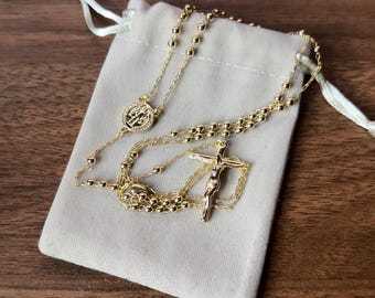 May include: A gold-toned rosary necklace with a small cross and a round pendant featuring a religious image. The necklace is displayed on a white velvet pouch.