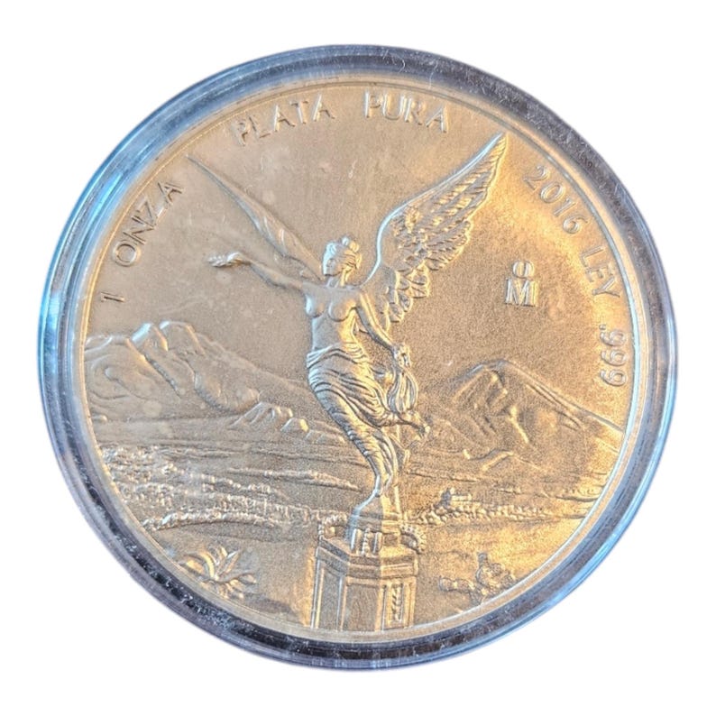 May include: Silver Libertad coin with the image of the Angel of Independence on the obverse. The coin is in a clear plastic capsule. The coin is dated 2016 and has the inscription "1 ONZA PLATA PURA 999 LEY".