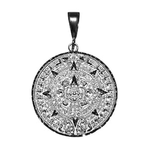 May include: A circular silver-toned pendant featuring a detailed relief of the Aztec sun stone calendar. The center displays a face with a protruding tongue, surrounded by concentric rings of intricate glyphs and symbols, topped with a bail.